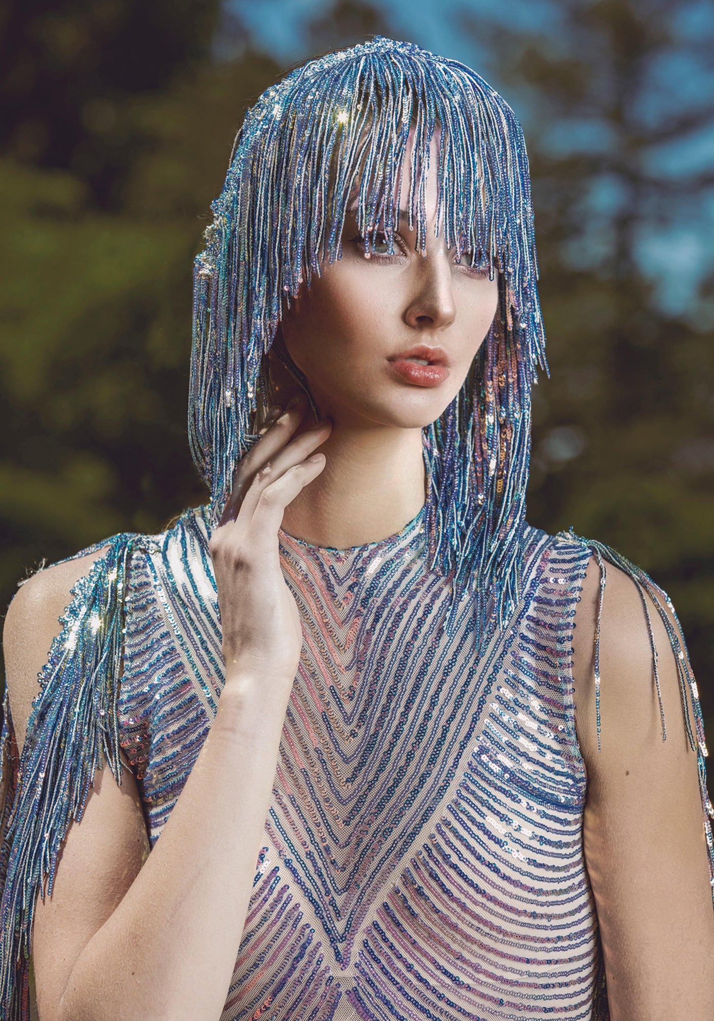 Model wearing a shimmering blue beaded fringe dress and headpiece, sparkling in natural outdoor light.